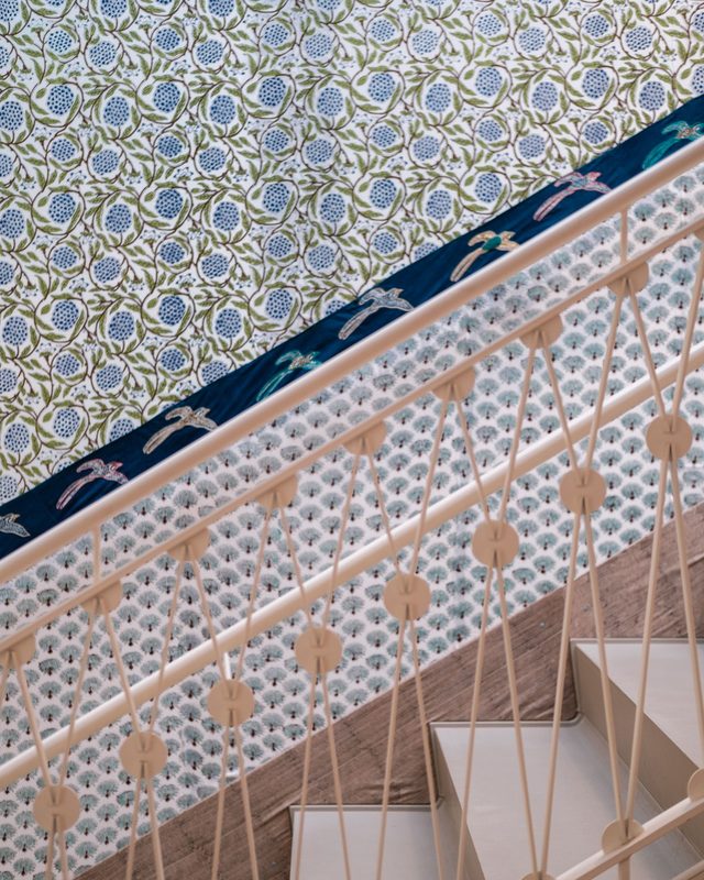 Stairwell seen from above with a blue and green botanical wallpaper running along a cream decorative railing and white steps