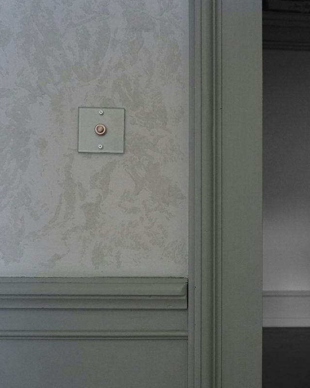 Close detail of a soft grey-green mottled wallcovering meeting a painted chair rail, wainscot panel and door casing