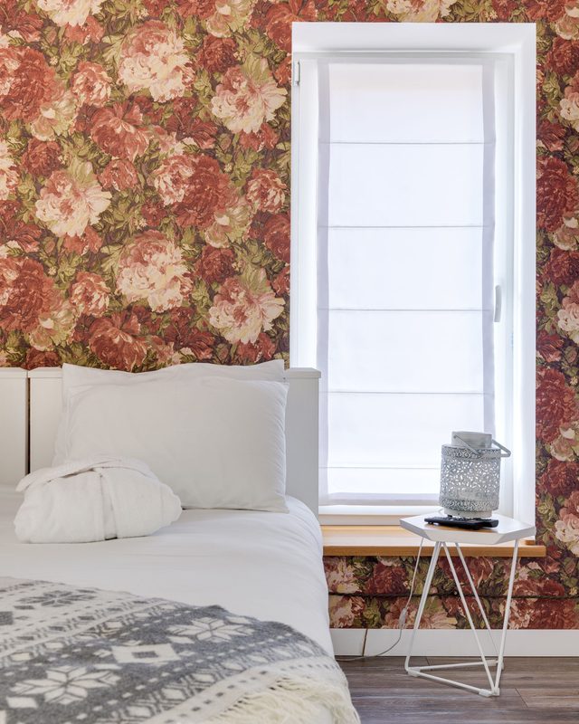 Bedroom with large red and blush peony wallpaper wrapped around a tall window beside a white bed