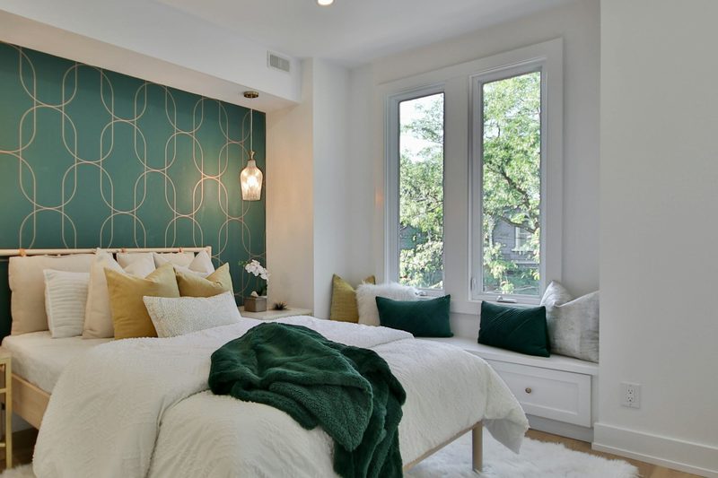 Bright bedroom with a deep teal feature wall patterned in fine gold arches behind the bed, beside a white window seat