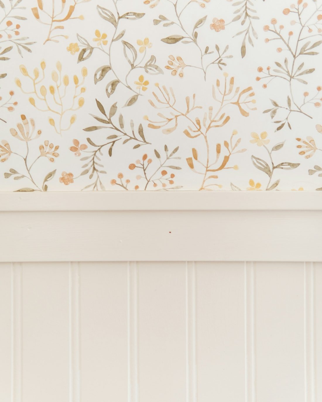 Cream watercolor botanical wallpaper meeting a white chair rail above beadboard wainscoting in a clean, straight line